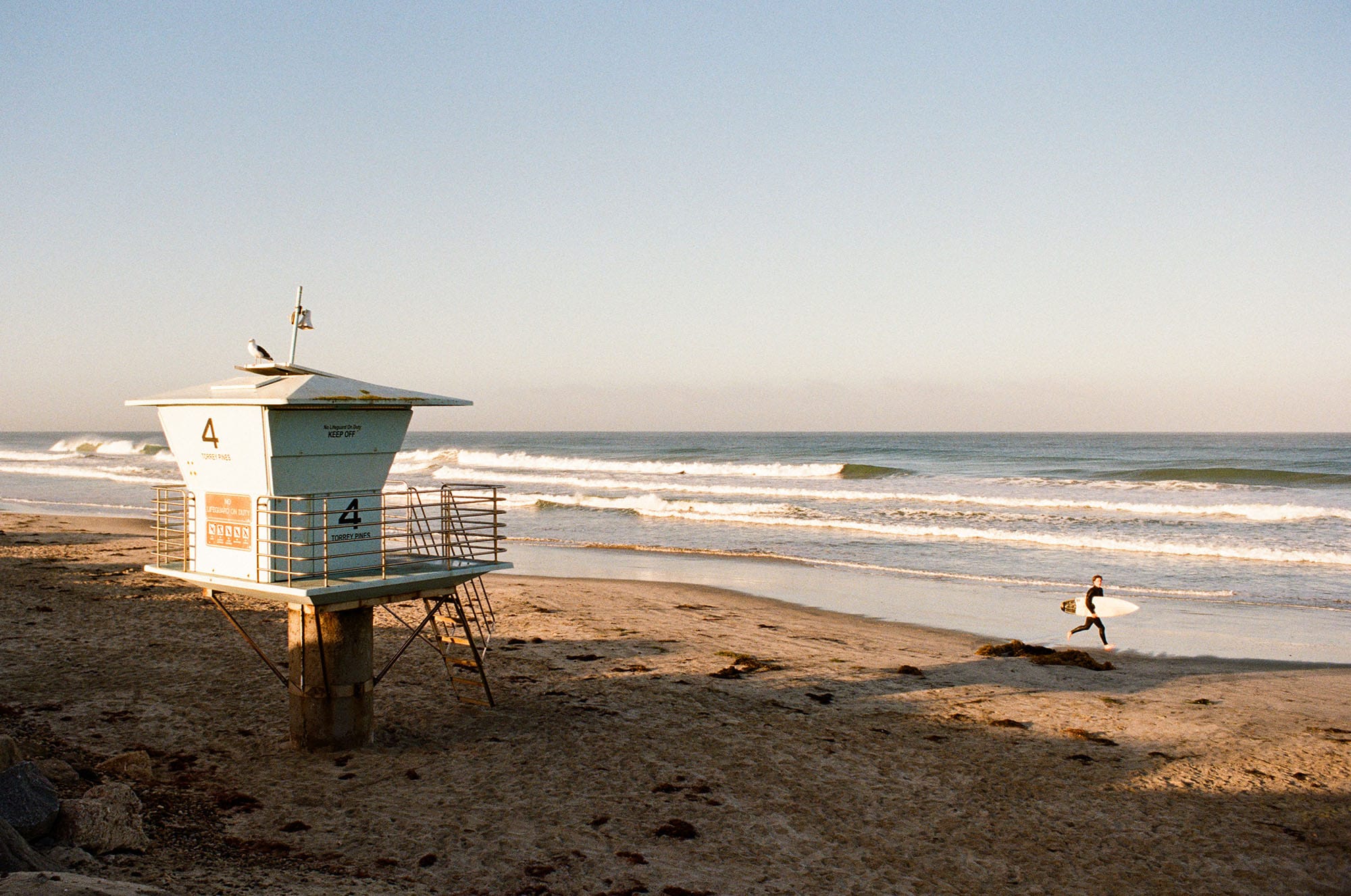Lifeguard tower on empty beach at sunset with surfer running along shoreline.