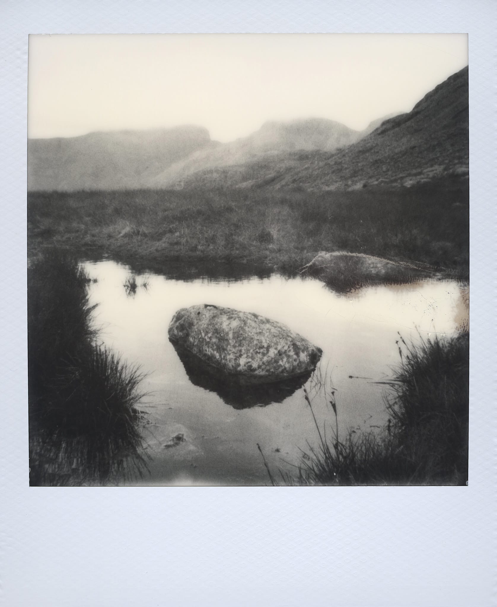 Moody mountain scene with small body of water and atmospheric lighting through fog.