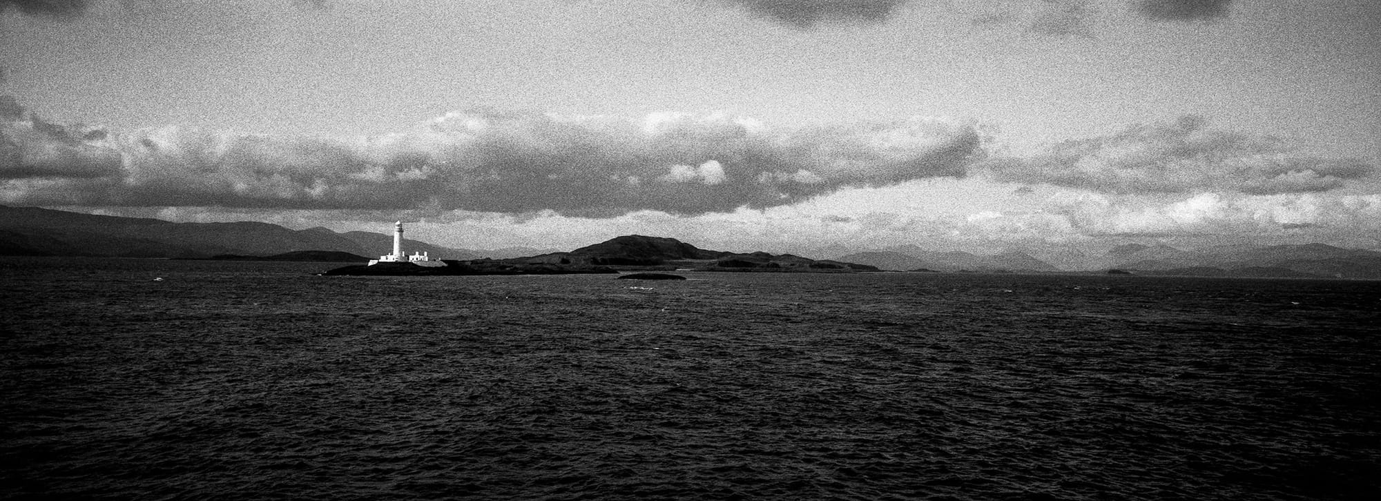 White lighthouse stands on dark island under dramatic cloud formation.