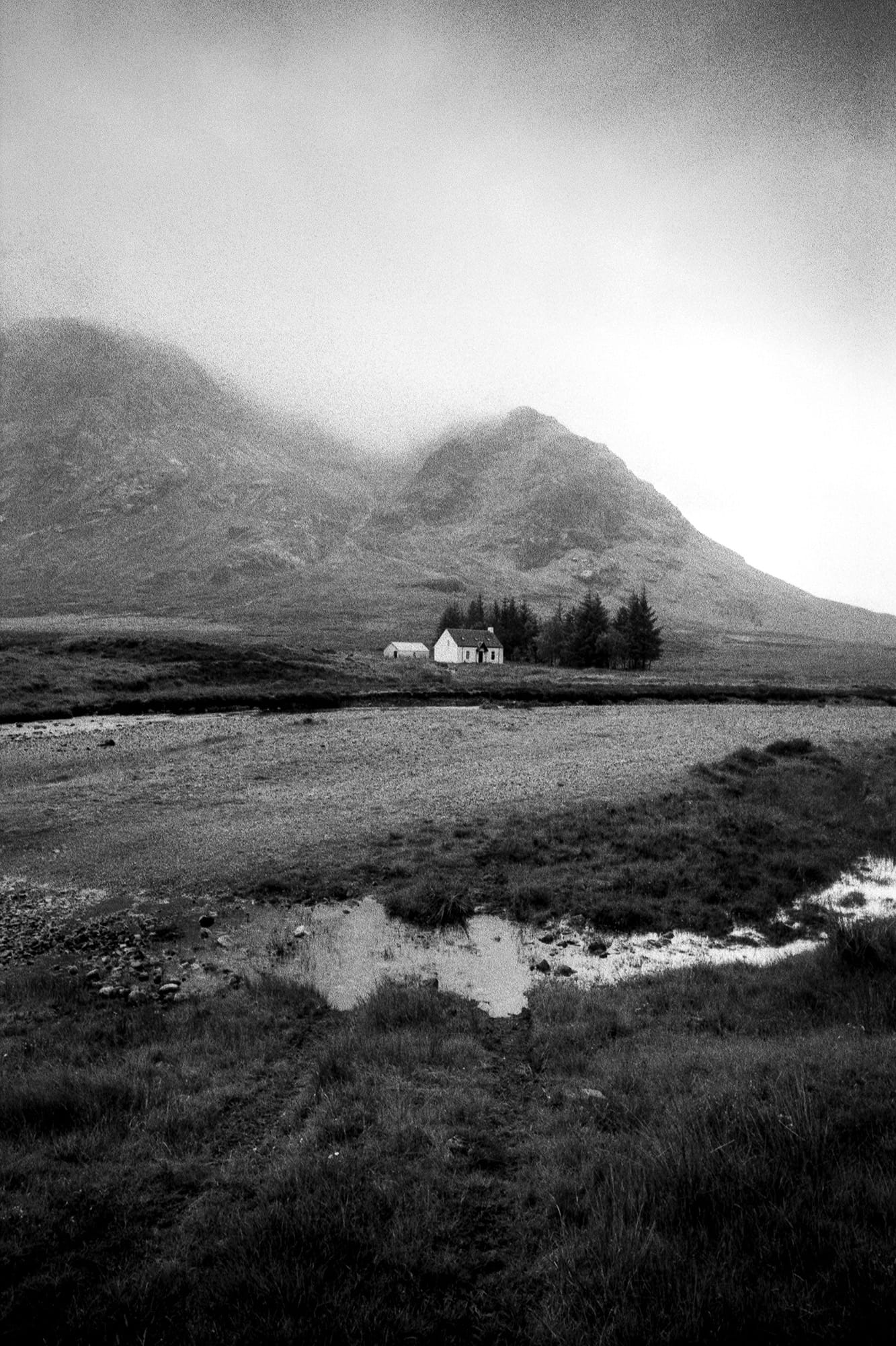 A house sits beneath mountain slope with a serene creek.
