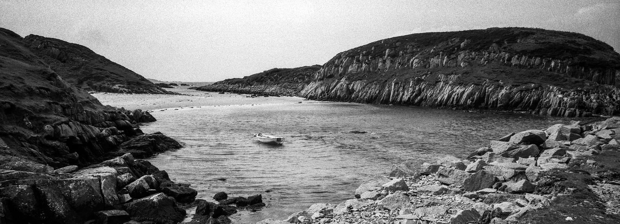 Small boat floats in rocky cove between steep coastal formations.