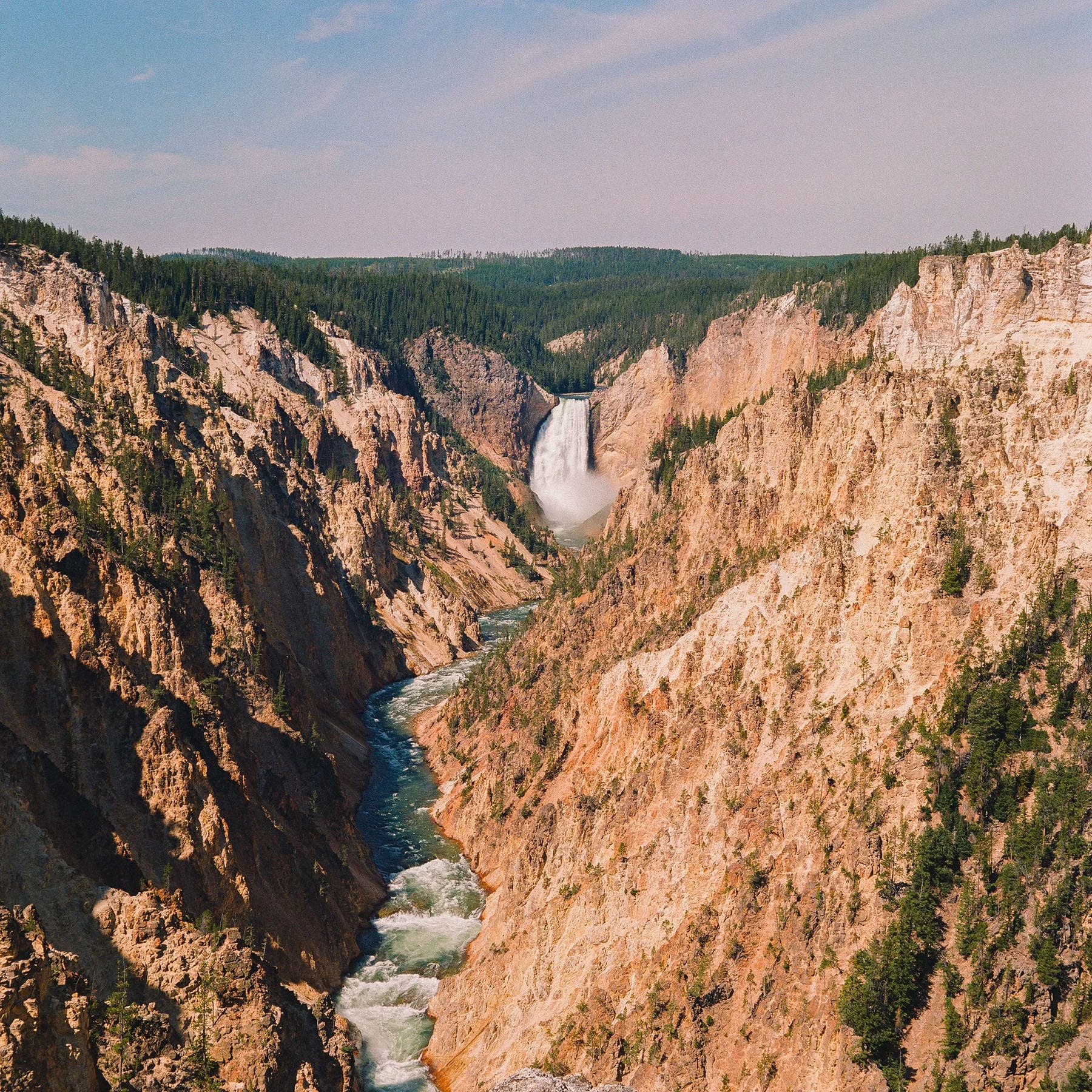 Yellowstone waterfall drops through orange canyon walls with river below.