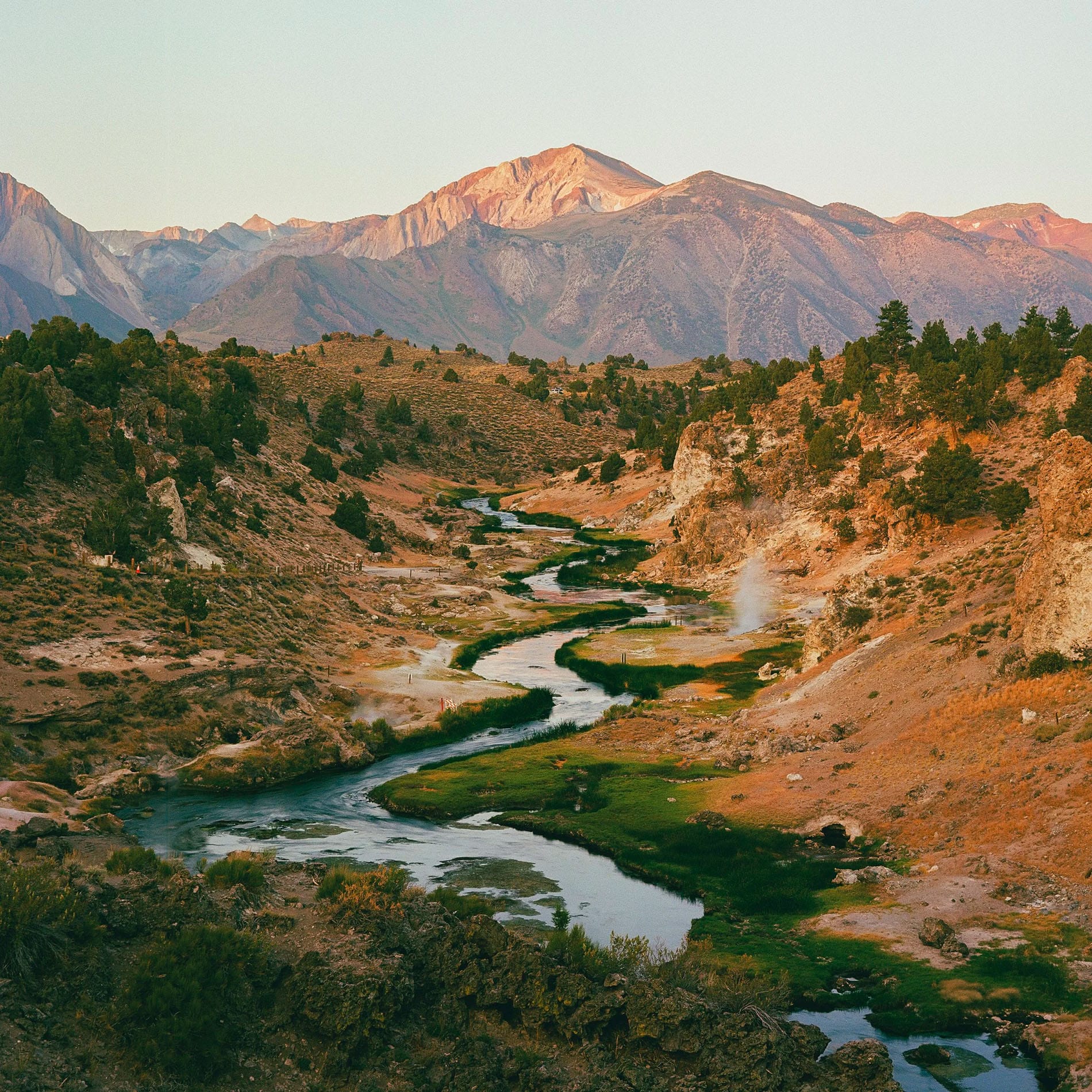 Geothermal stream winds through California valley with mountains in warm evening light.
