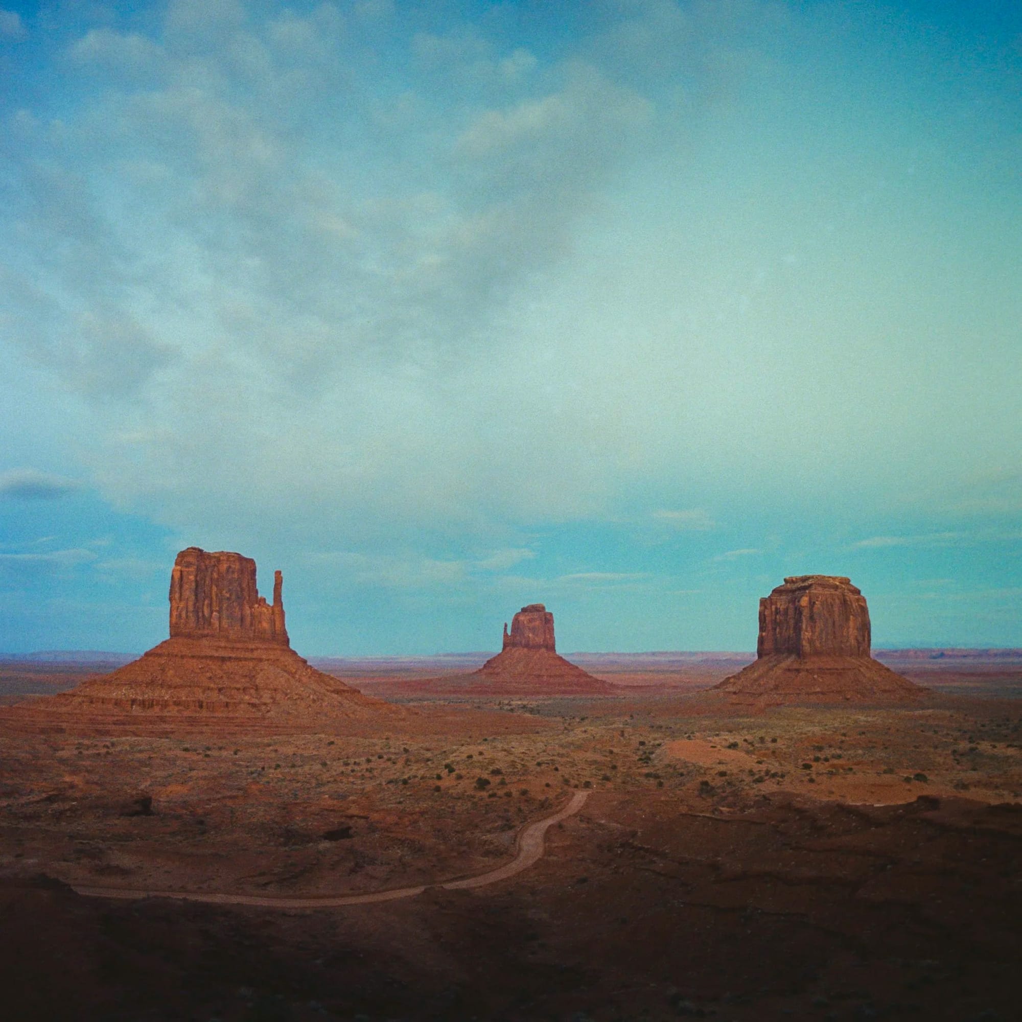 Three Monument Valley buttes stand under blue sky in desert landscape.