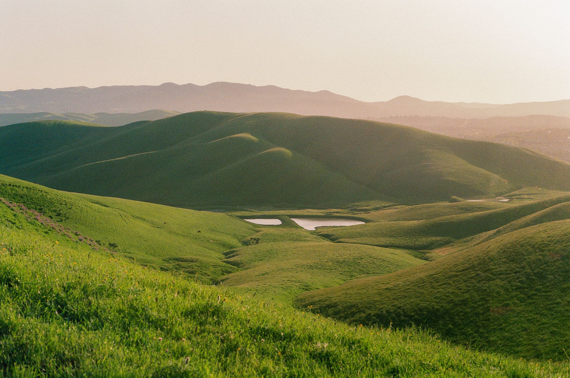 Green hills fold into valley with small lake at sunset.