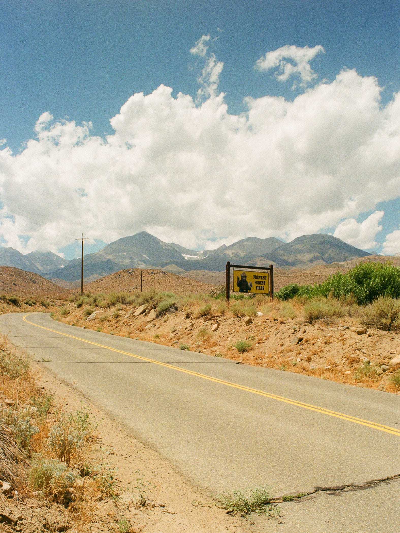 Desert highway curves past Inyo National Forest sign with mountains ahead.