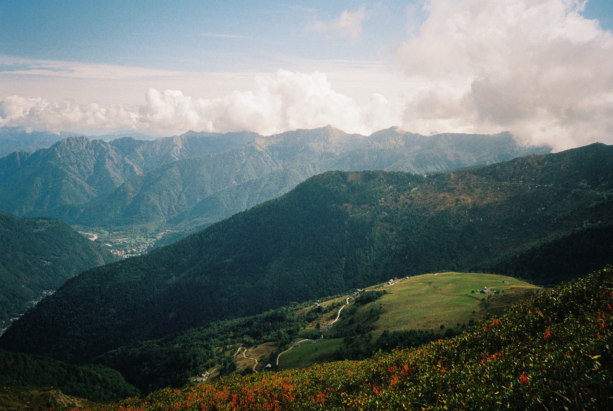 Mountain valley panorama with green hills winding road and dramatic clouds on color film.