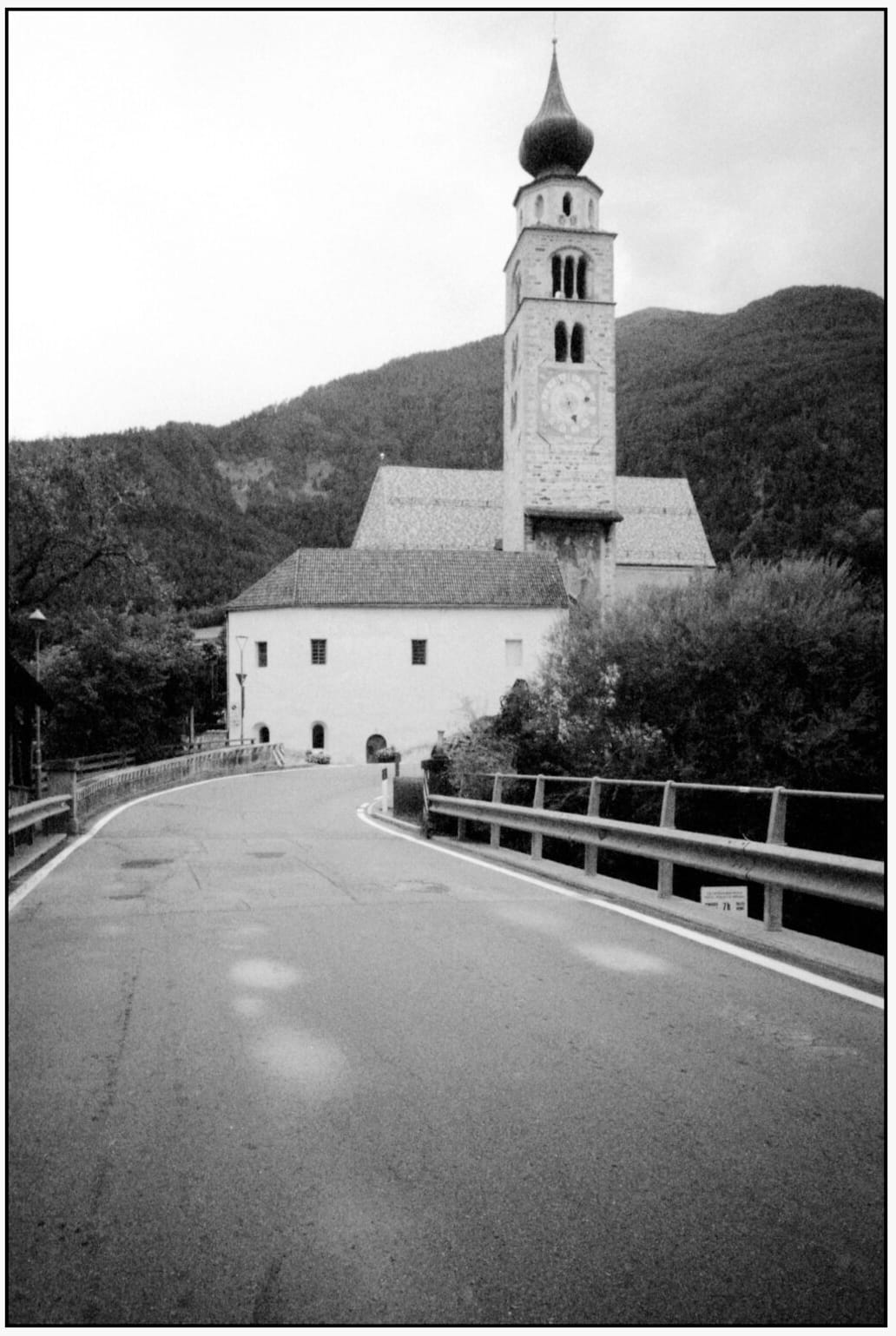 Alpine church with onion dome stands at end of curved mountain road.