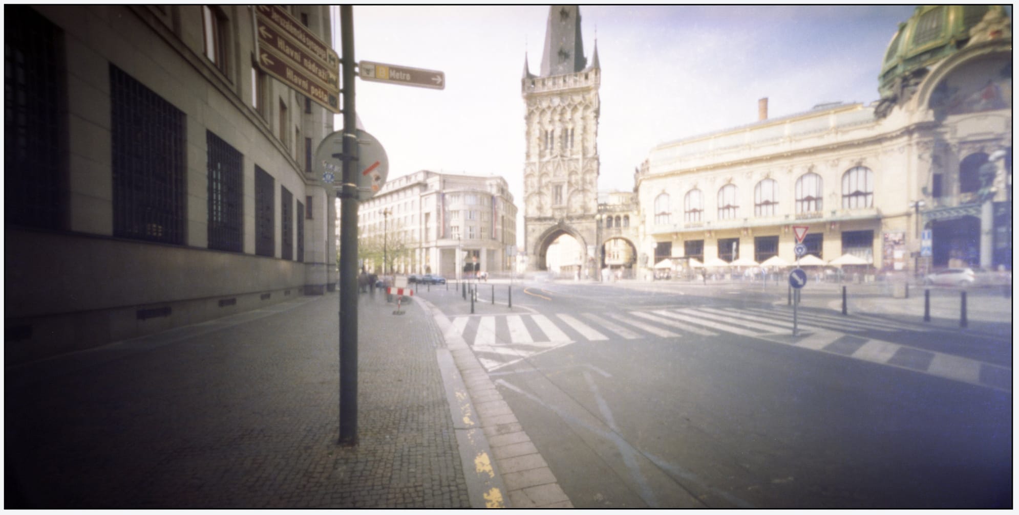 Prague street corner shows historic tower and crosswalk in soft focus.