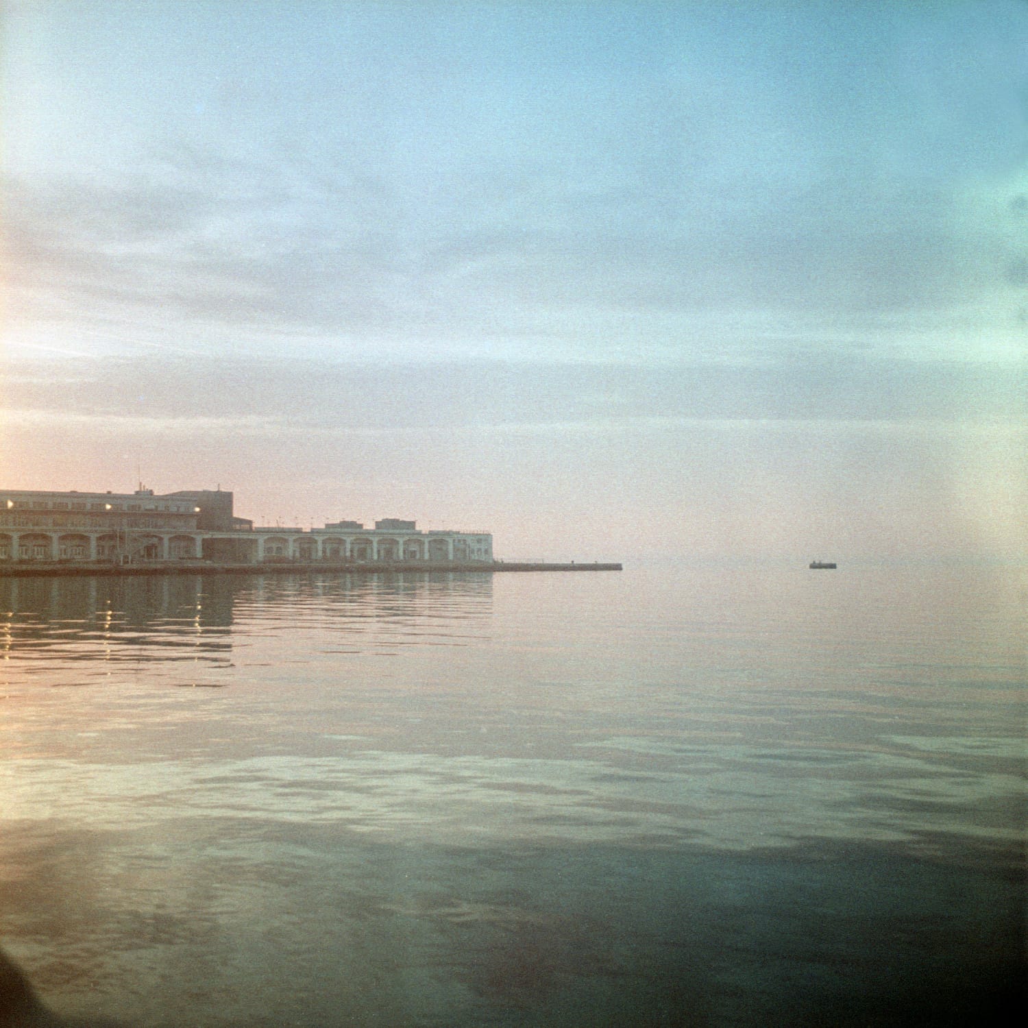 Waterfront building reflects in calm turquoise water at dawn.