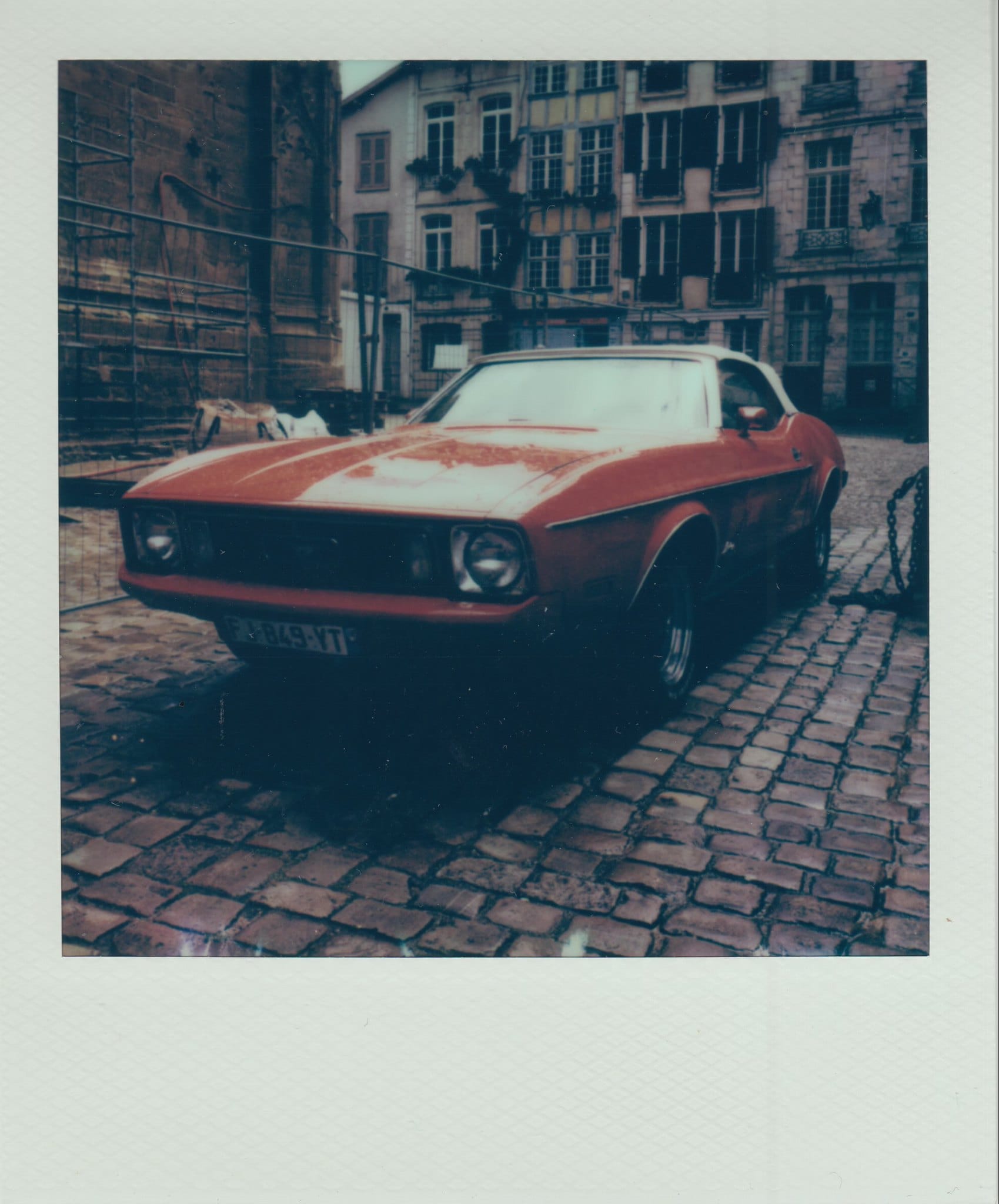 Red Ford Mustang on cobblestone street with European apartment buildings in Polaroid frame.