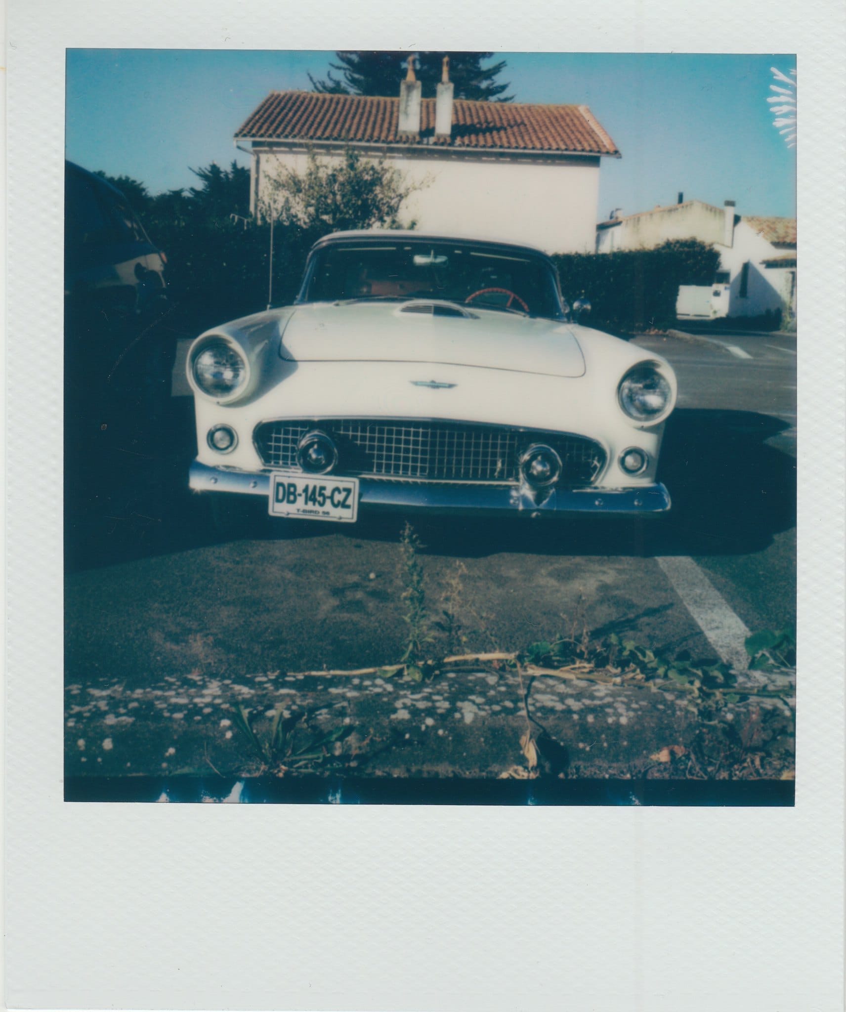 White Ford Thunderbird on residential street with Mediterranean house in Polaroid frame.