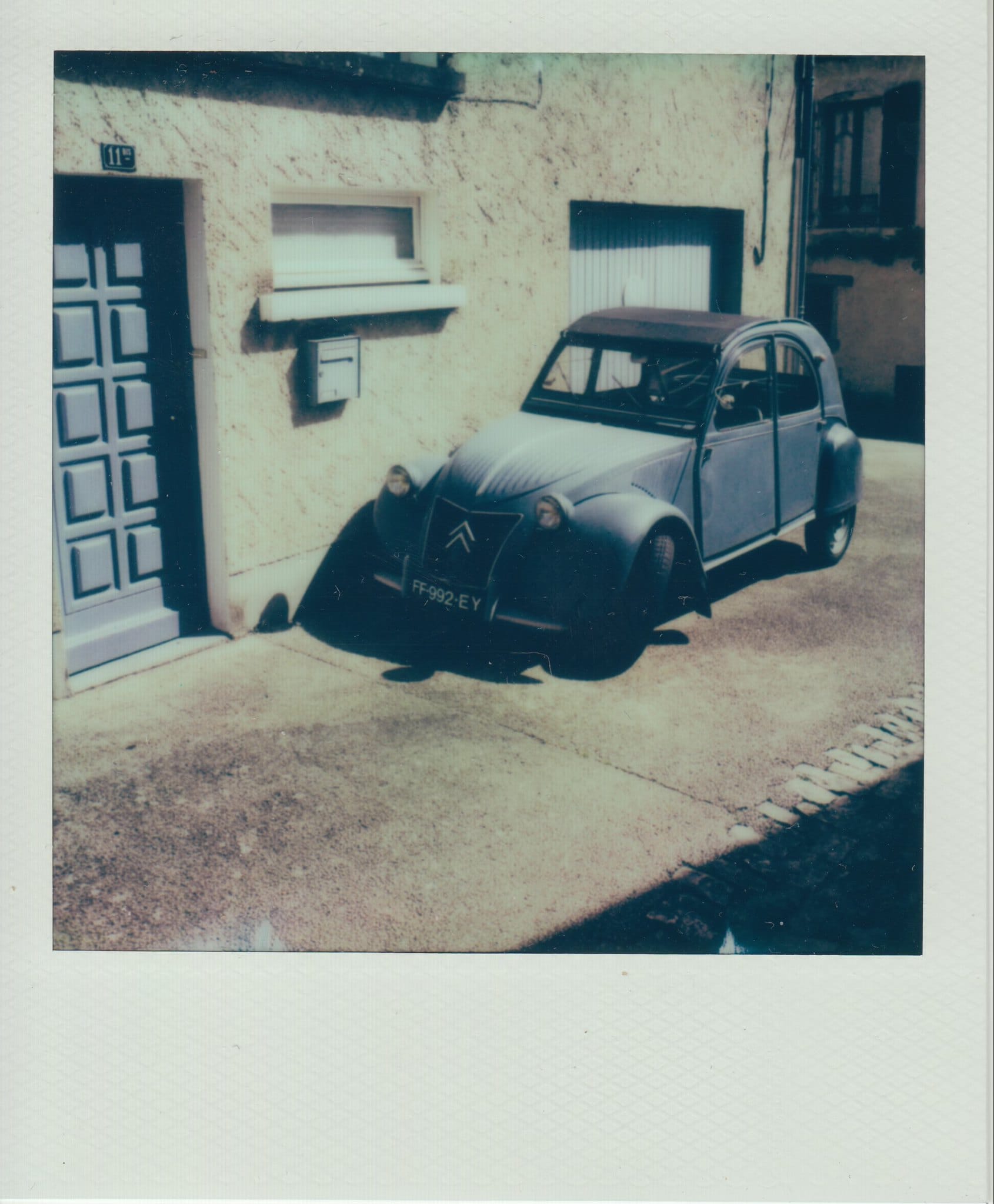 Gray Citroën 2CV on street with blue building door in faded instant film photo.