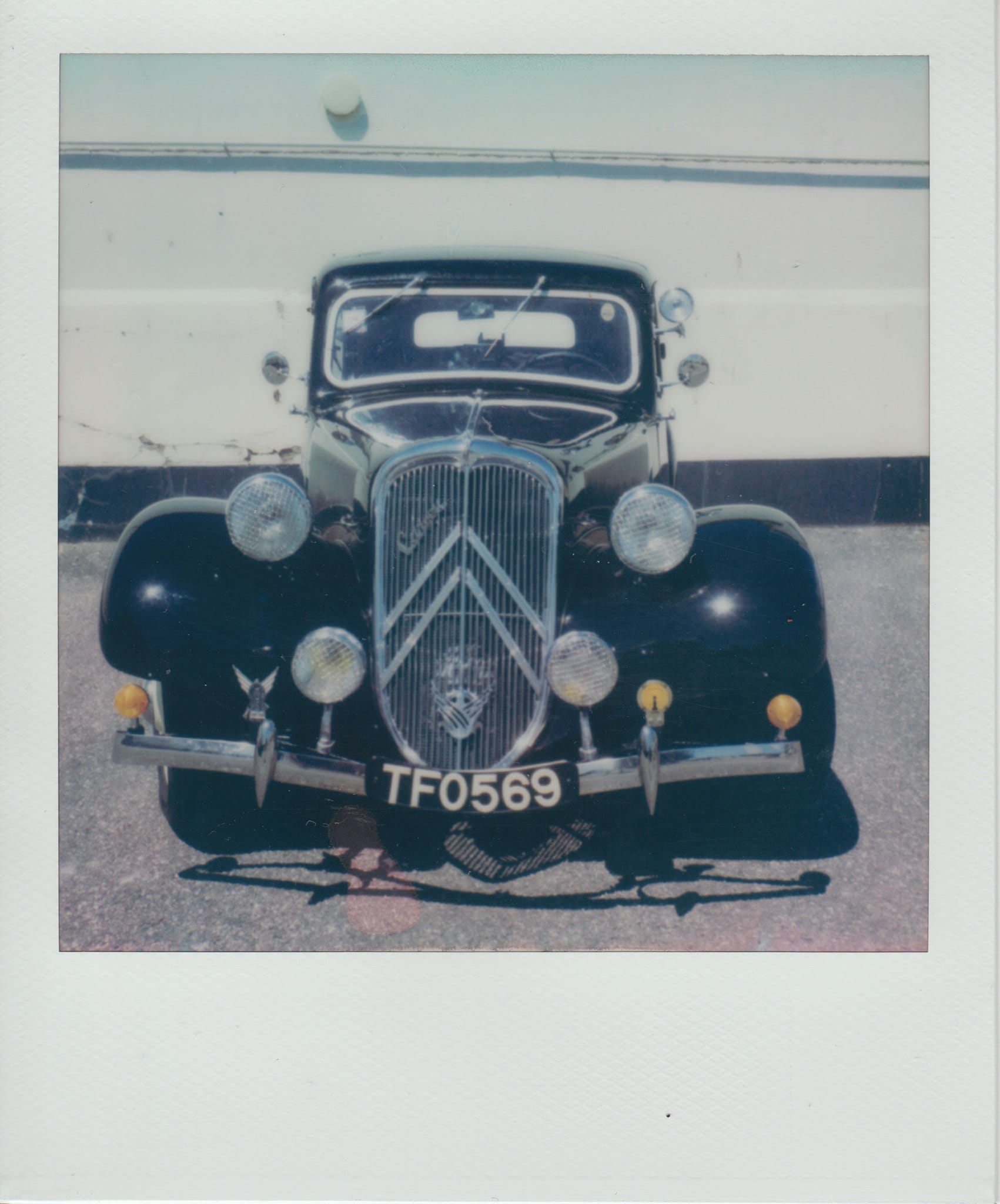 Black Citroën with chevron grille photographed head-on on asphalt in faded Polaroid.