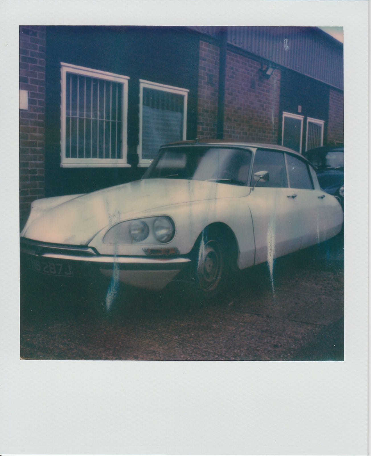 White Citroën DS with missing wheel against brick building instant film photo.