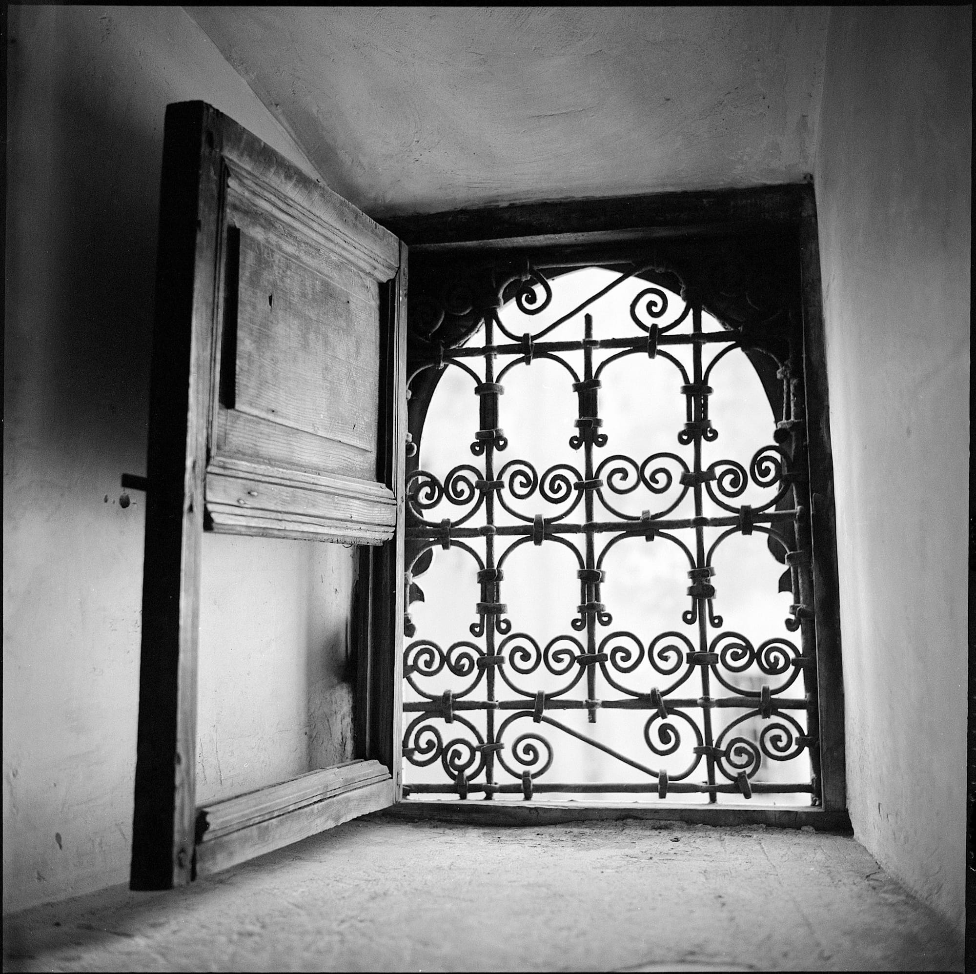 Ornate iron window grill framed by open wooden shutters.
