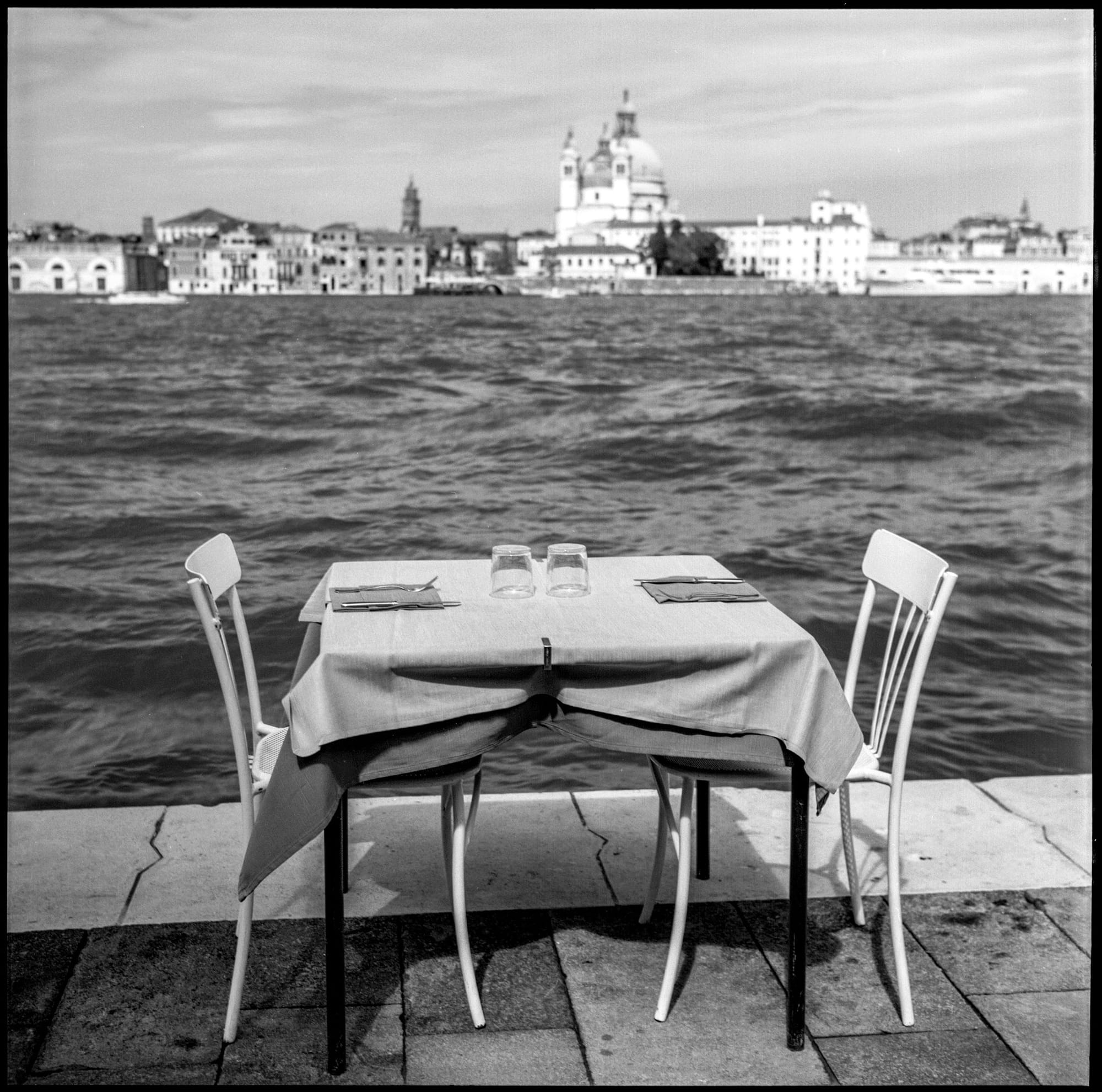 Empty restaurant table faces Venice skyline across choppy water.