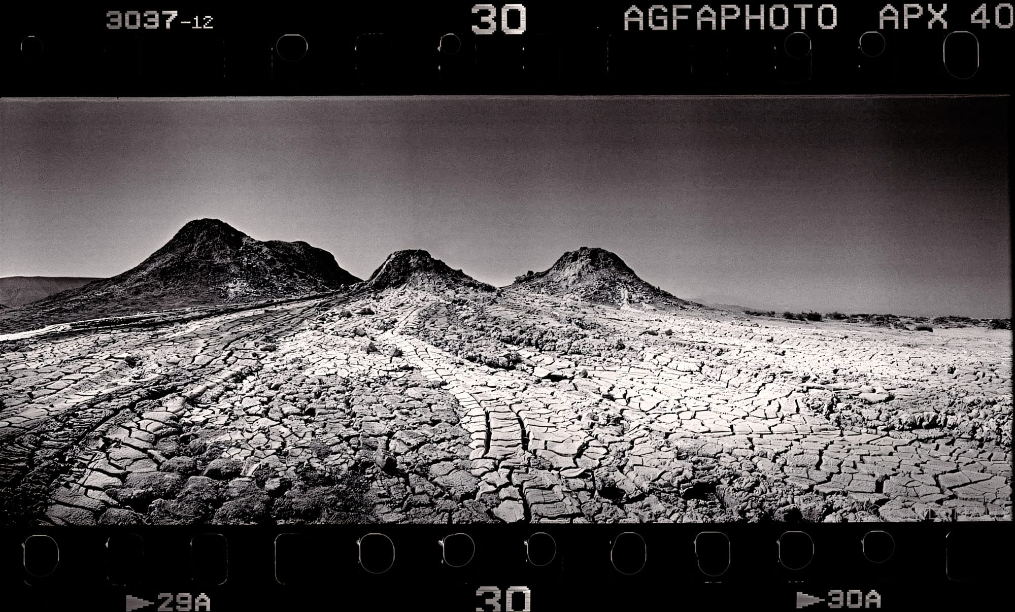 Cracked desert mud stretches toward distant mountains with visible film sprockets.