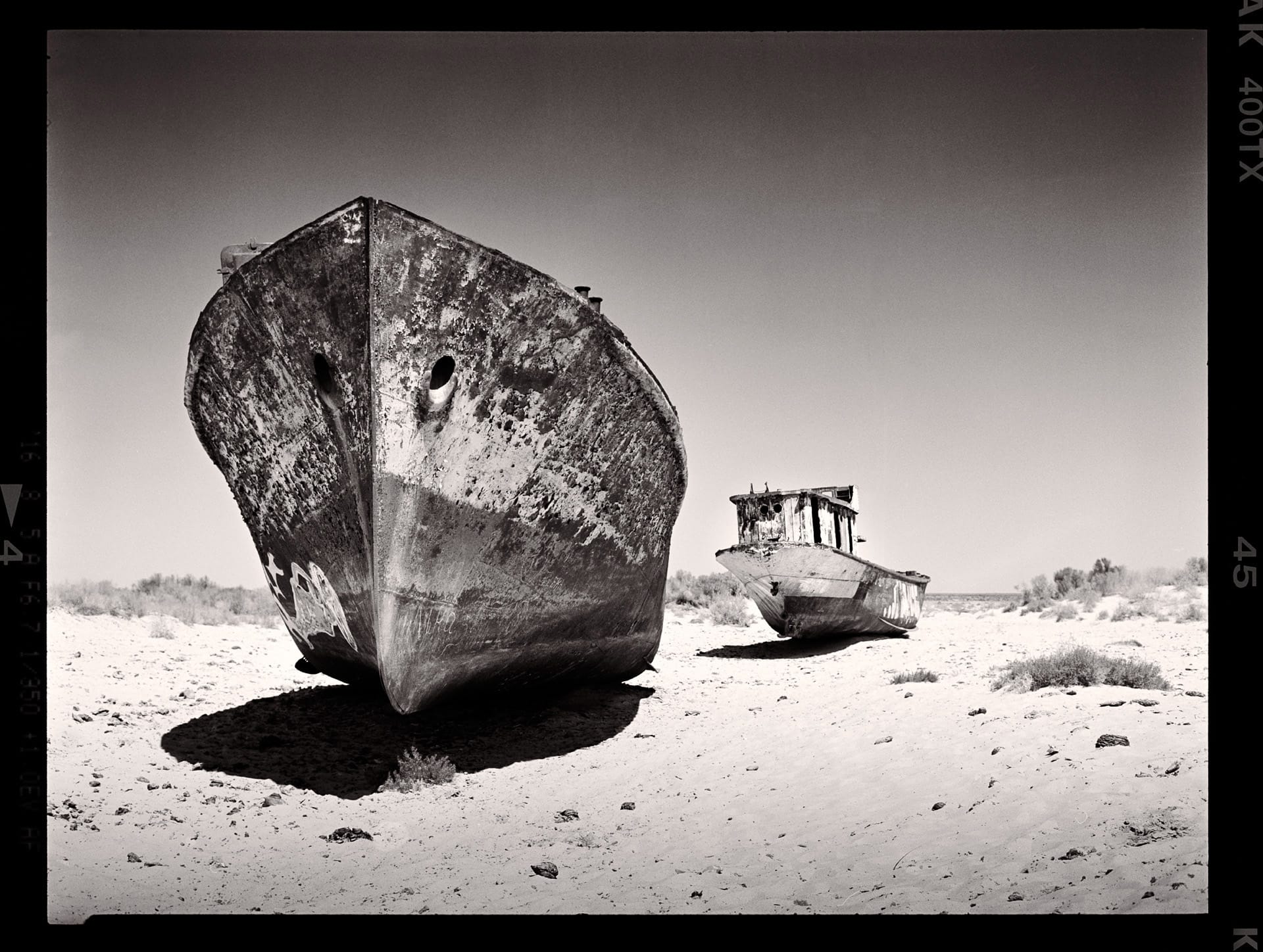 Rusted ship hulls rest on dry desert sand in harsh sunlight.