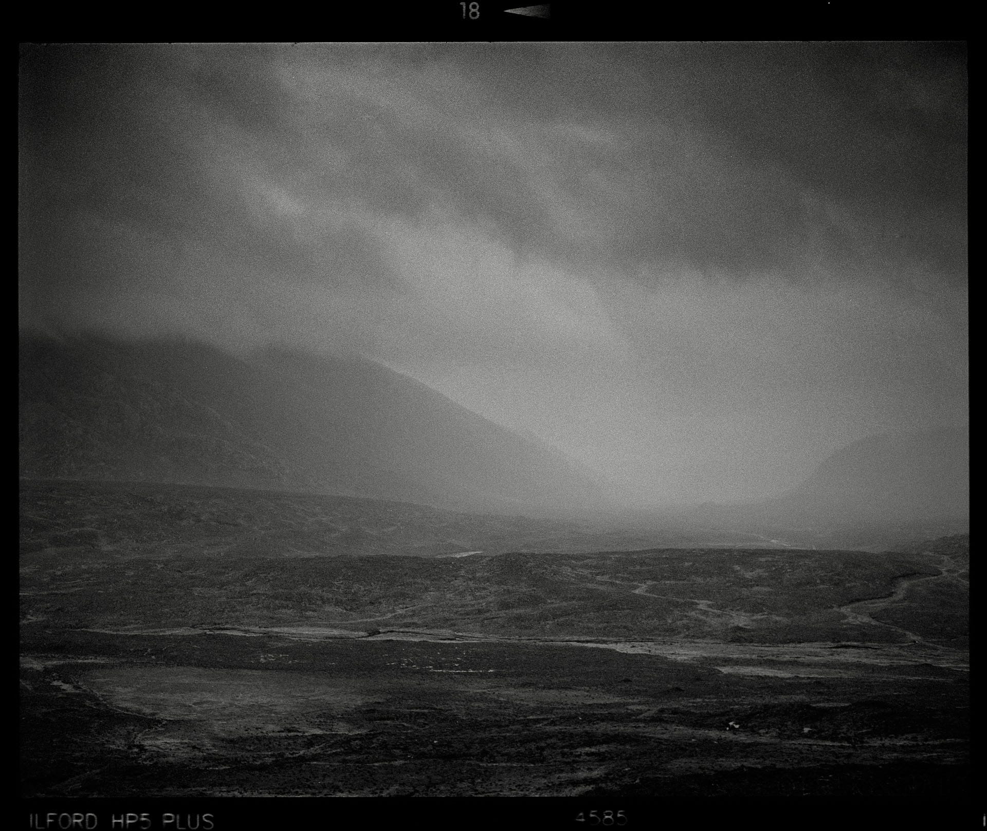 Dark moody landscape shows valley under heavy storm clouds.