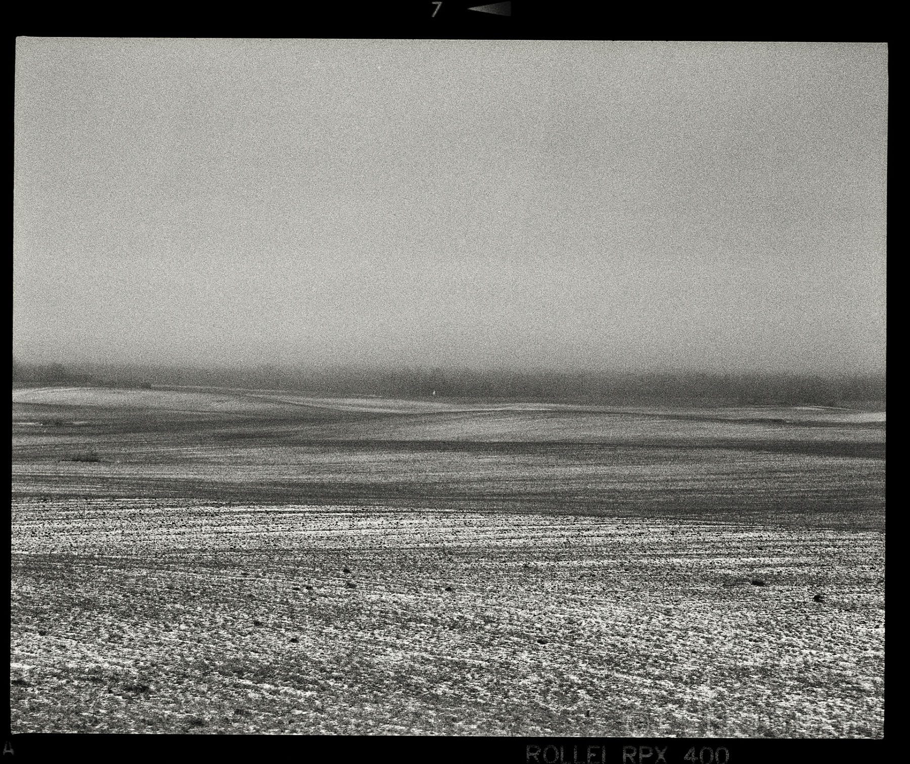 Minimalist seascape shows textured water surface under overcast sky with film edge.