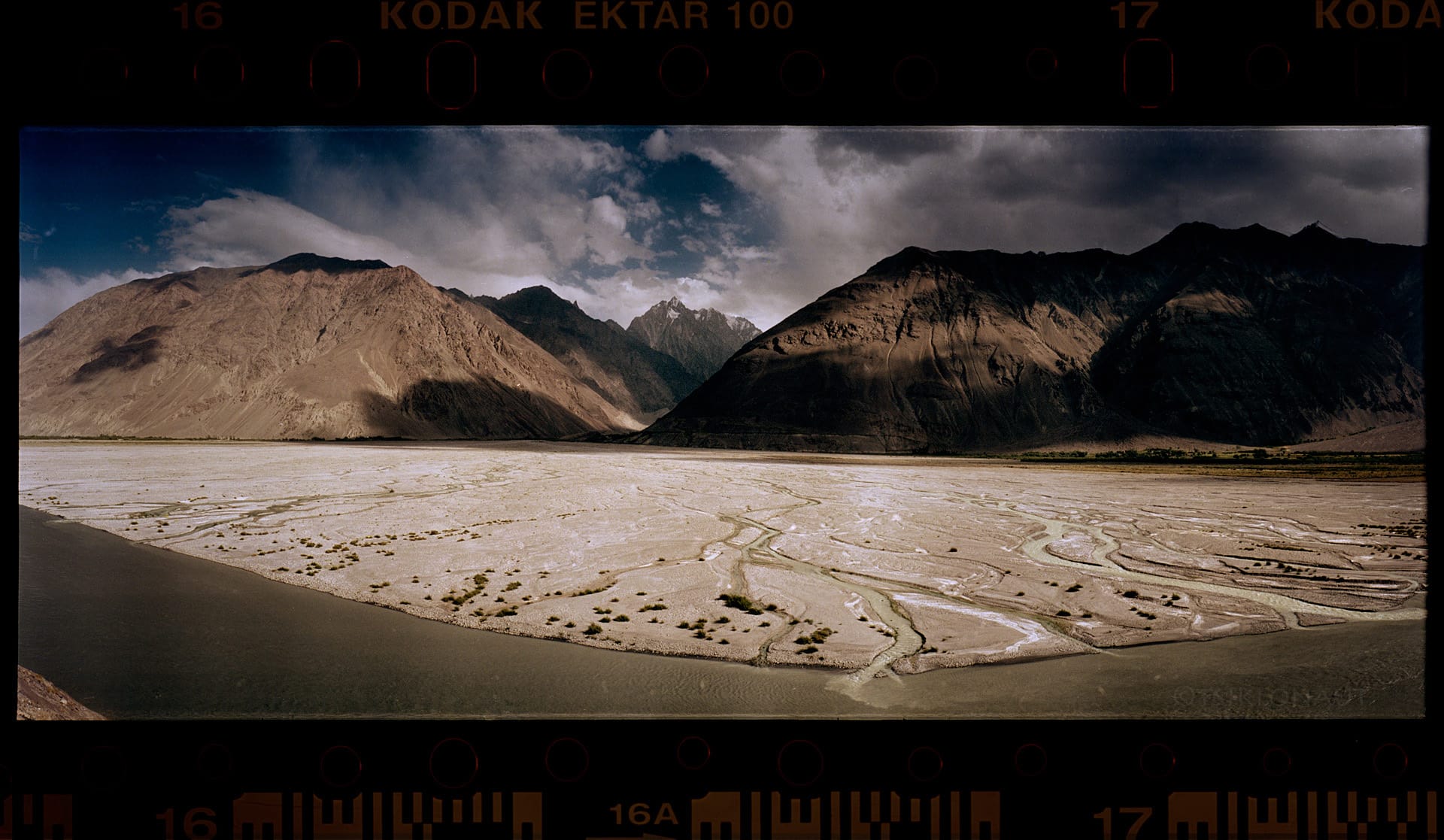 River valley winds through mountains under dramatic clouds with visible Kodak film border.