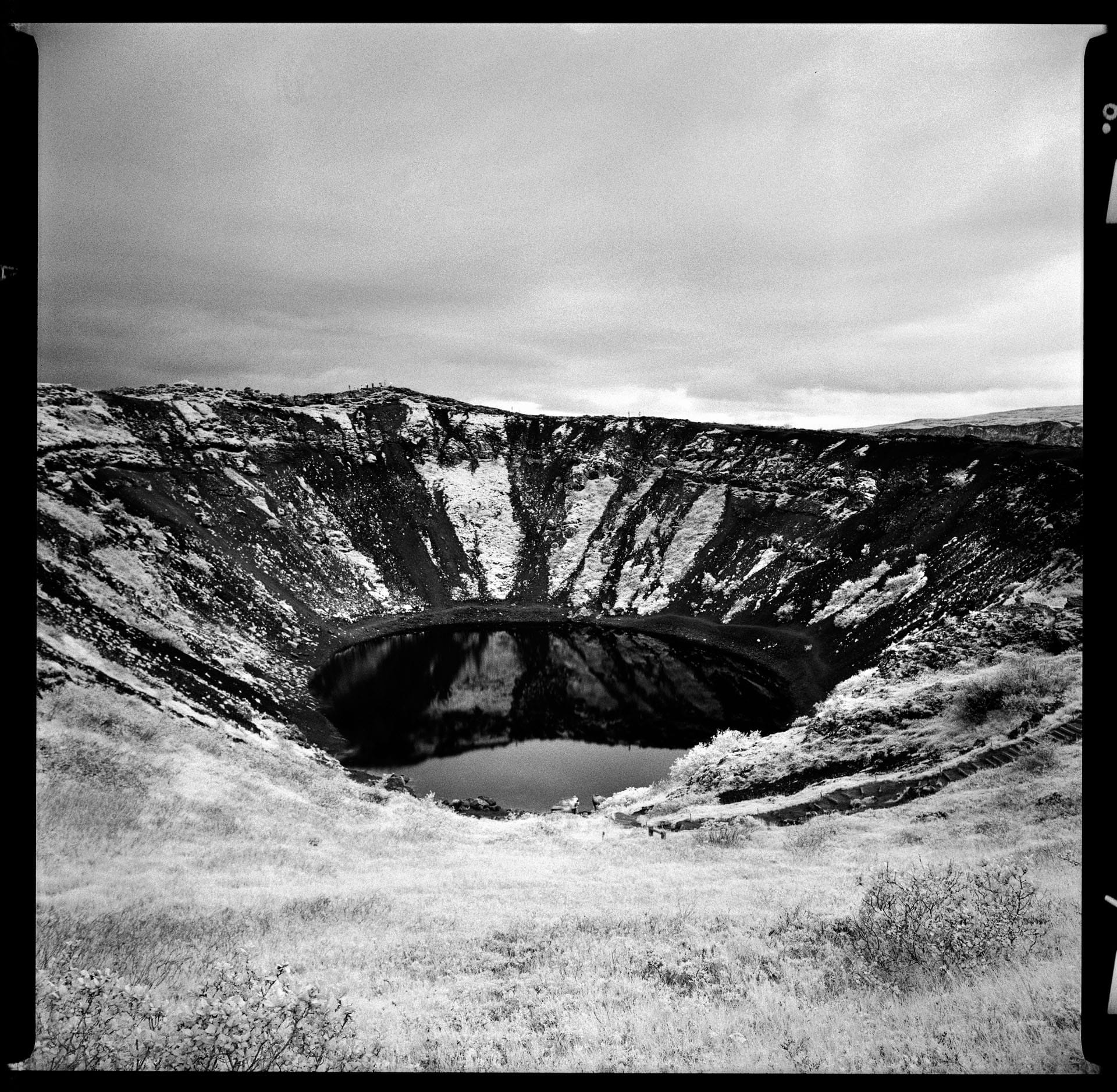 Volcanic crater lake reflects snow-covered walls in black and white.