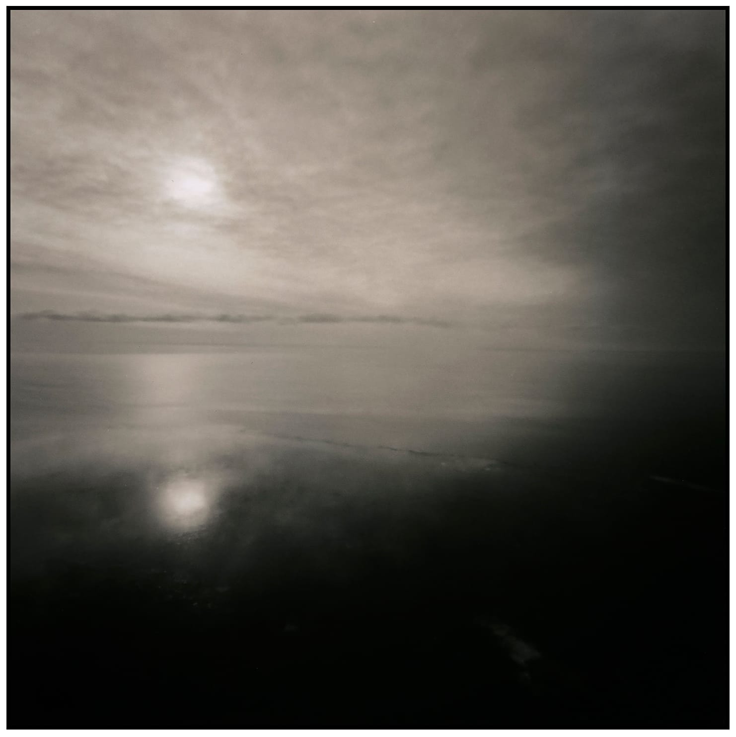 Long exposure of misty ocean with sun reflection creating soft gradient from dark water to pale sky.