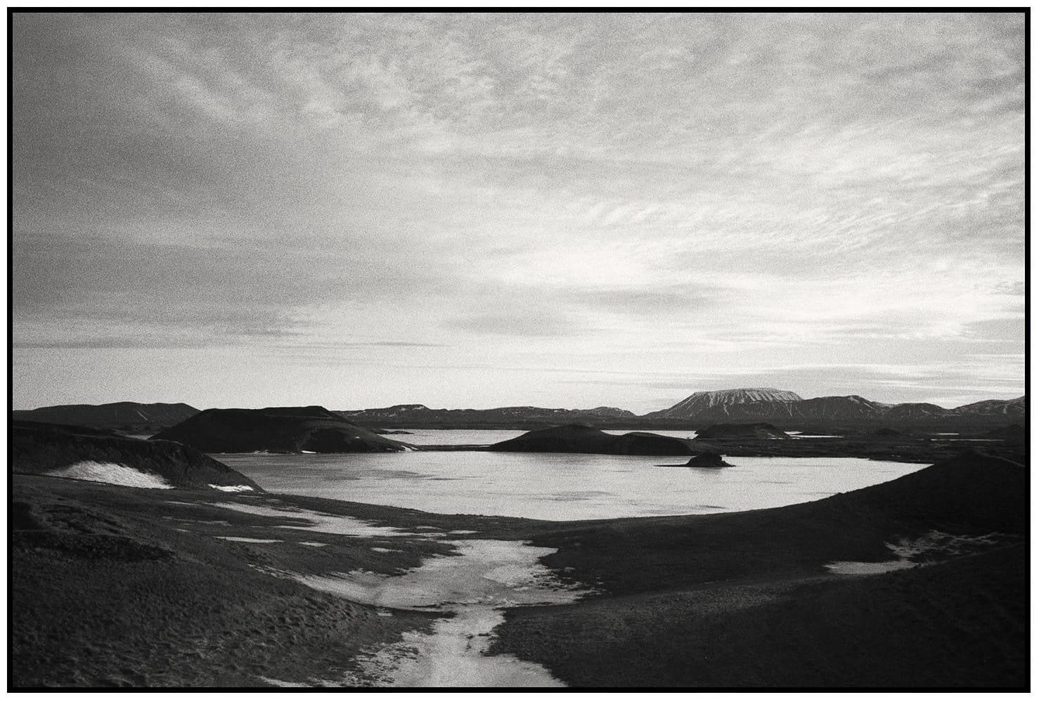 Panoramic view of volcanic crater lake with dark mountains silhouetted against textured sky.