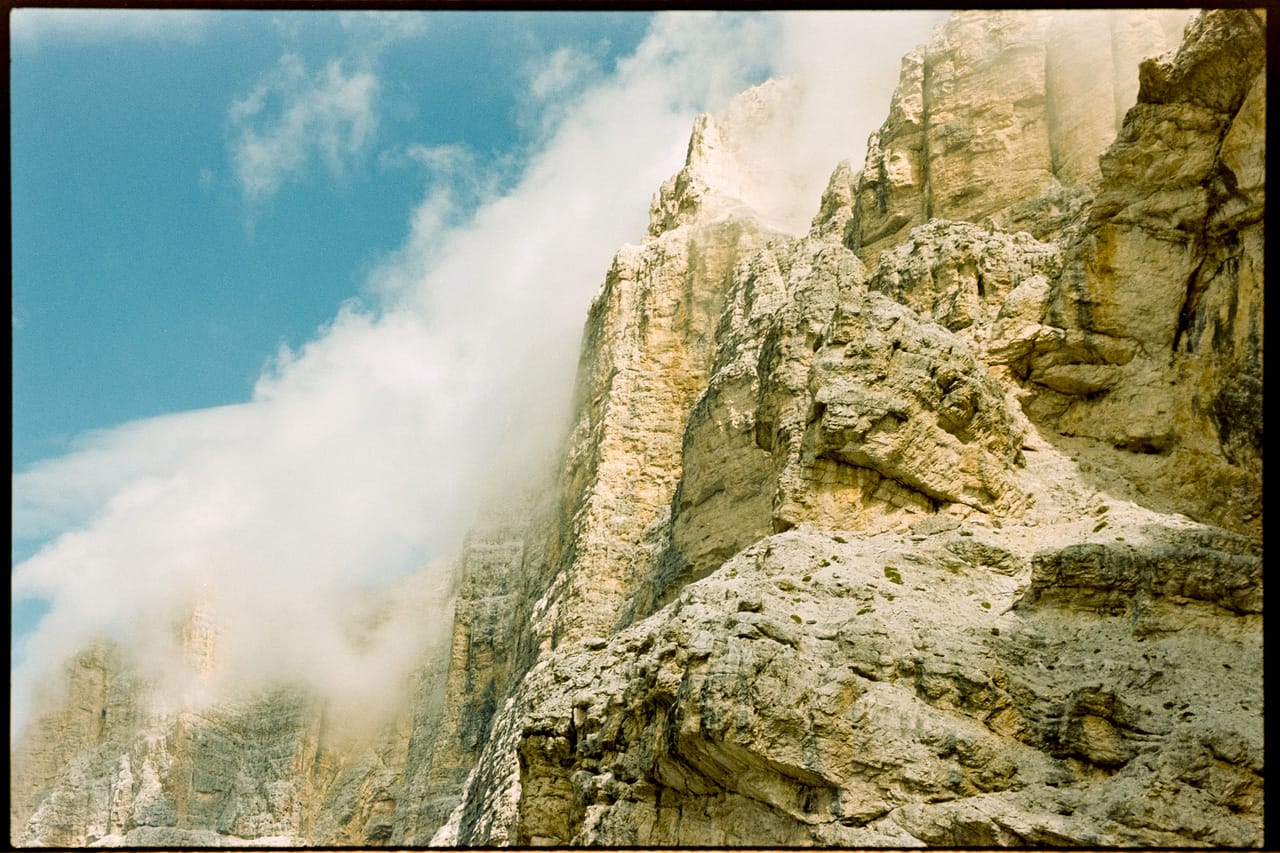 Dramatic mountain cliff face with light leak and clouds shot on color film.