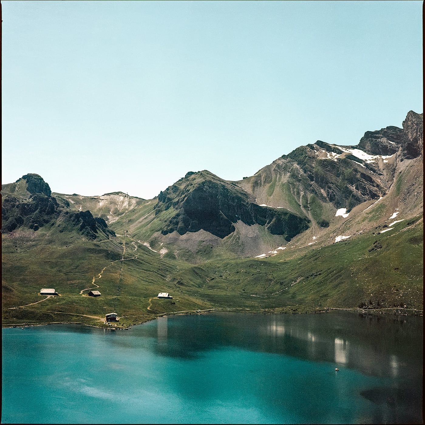 Alpine lake with turquoise water reflecting mountains and small buildings on hillside.