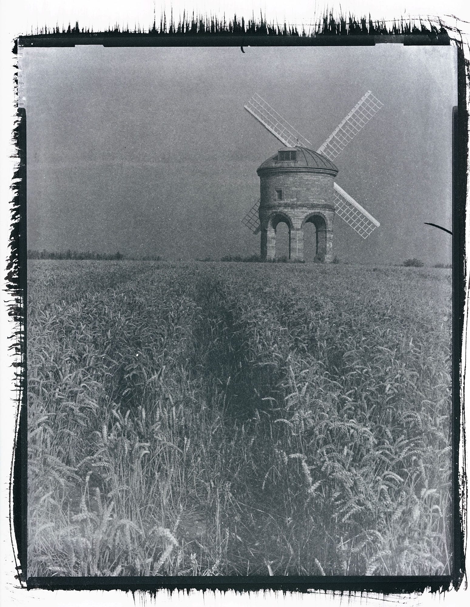 Stone windmill in wheat field against overcast sky black white large format.